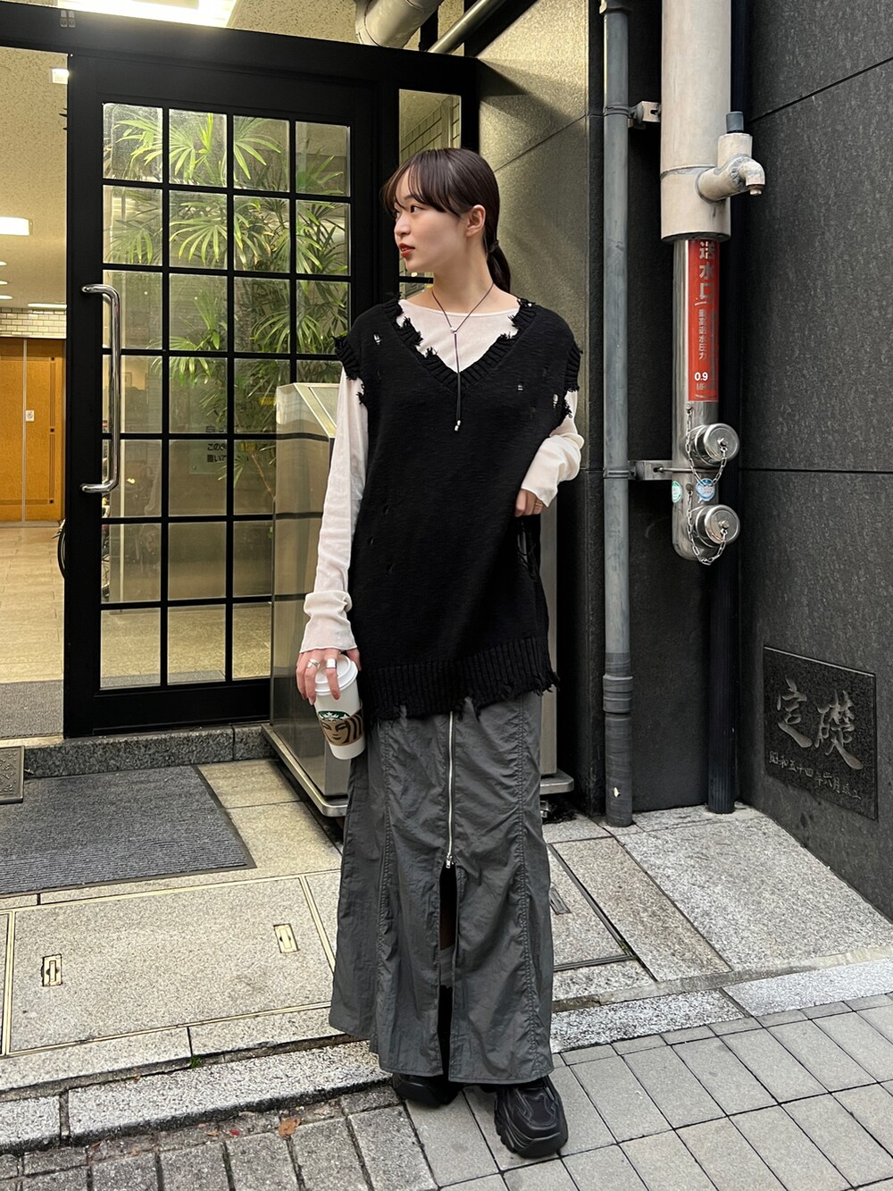 グレー系のスカート、ブラック系のベスト、ブラック系のスニーカーを着用したレディースの冬コーディネートの2枚目の写真