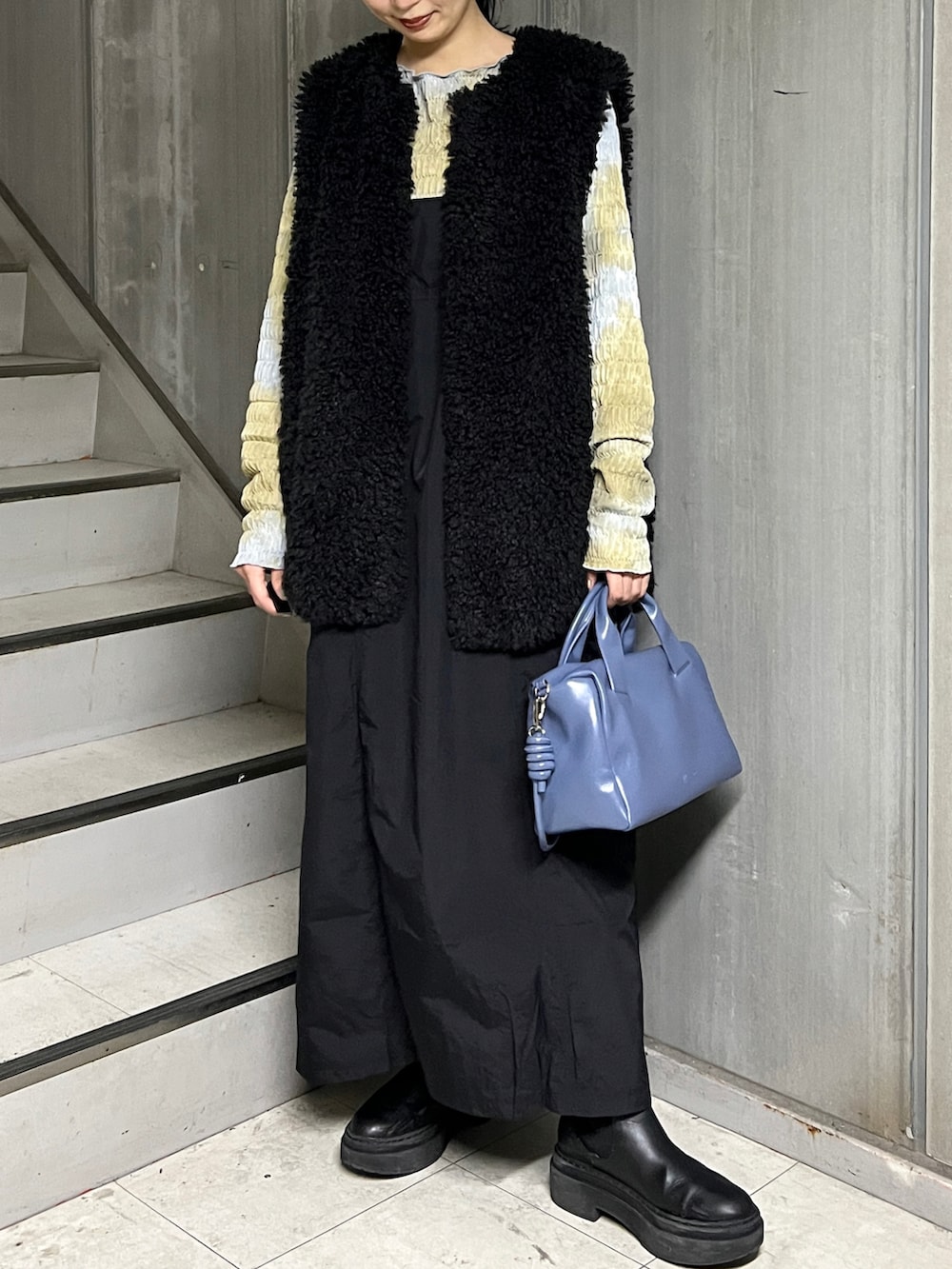 ブラック系のベスト、ブルー系のボストンバッグ、ブラック系のワンピースを着用したレディースの秋コーディネートの2枚目の写真