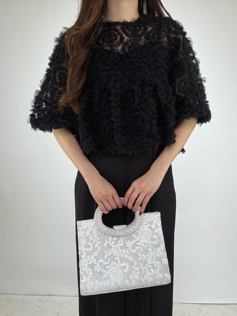 シルバー系のクラッチバッグ、シルバー系のパンプス、ブラック系のドレスを着用したレディースの秋コーディネートの4枚目の写真