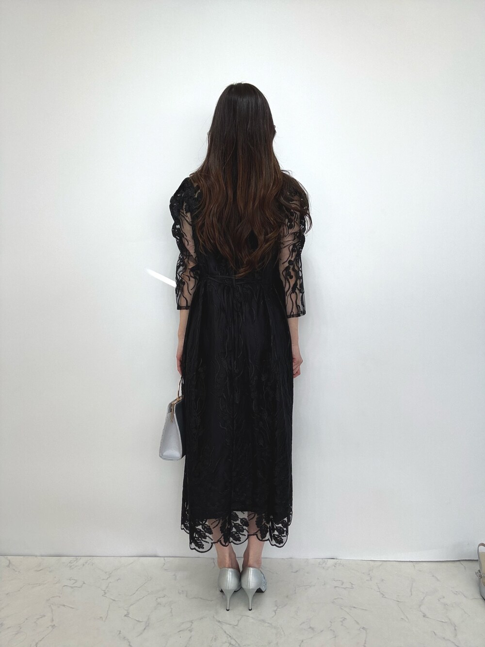 ブラック系のドレス、シルバー系のクラッチバッグ、シルバー系のパンプスを着用したレディースの秋コーディネートの3枚目の写真