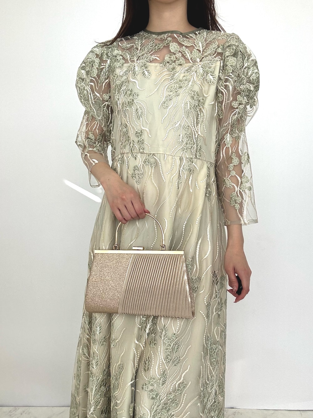 グリーン系のドレス、ベージュ系のクラッチバッグ、ベージュ系のパンプスを着用したレディースの秋コーディネートの3枚目の写真