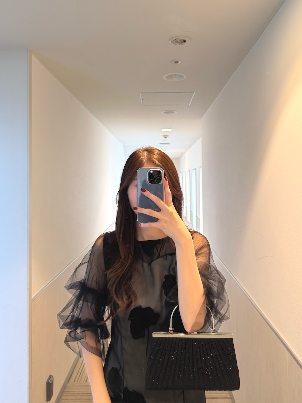 ブラック系のドレス、ブラック系のパンプス、ベージュ系のクラッチバッグを着用したレディースの秋コーディネートの4枚目の写真