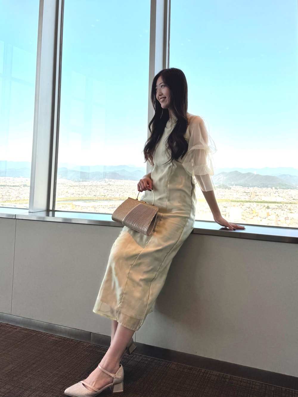 ベージュ系のクラッチバッグ、グリーン系のドレス、ベージュ系のパンプスを着用したレディースの秋コーディネートの2枚目の写真