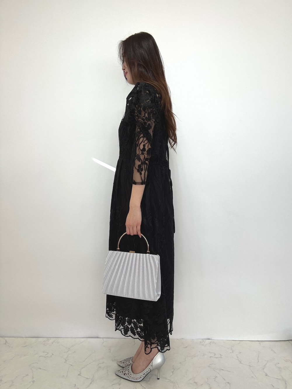 ブラック系のドレス、シルバー系のクラッチバッグ、シルバー系のパンプスを着用したレディースの秋コーディネートの2枚目の写真