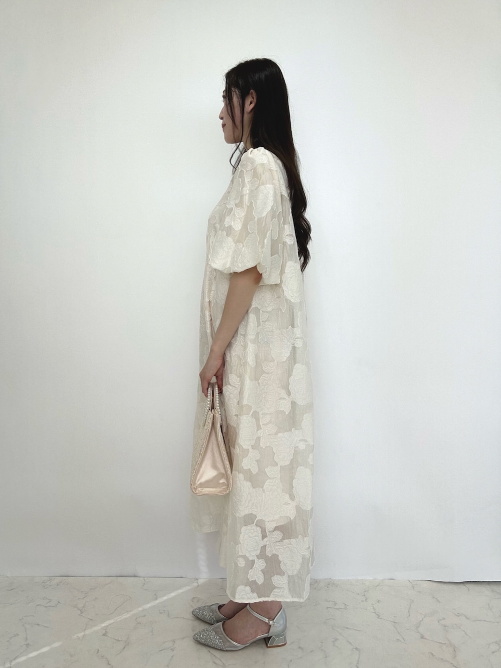 ベージュ系のドレス、ベージュ系のクラッチバッグ、シルバー系のパンプスを着用したレディースの秋コーディネートの2枚目の写真