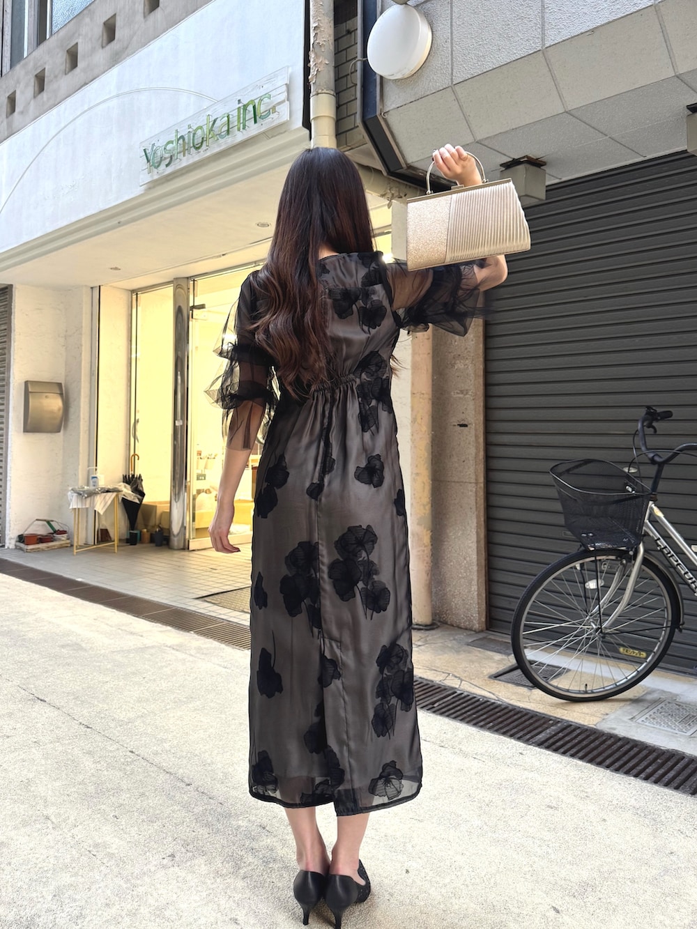 ブラック系のドレス、ブラック系のパンプス、ベージュ系のクラッチバッグを着用したレディースの秋コーディネートの2枚目の写真