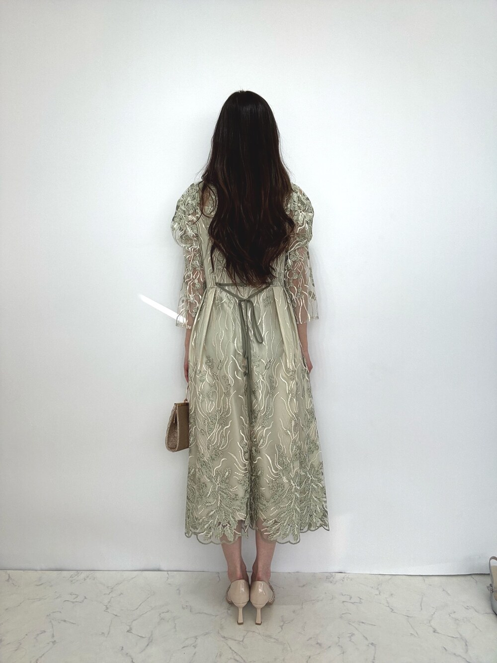 グリーン系のドレス、ベージュ系のクラッチバッグ、ベージュ系のパンプスを着用したレディースの秋コーディネートの4枚目の写真