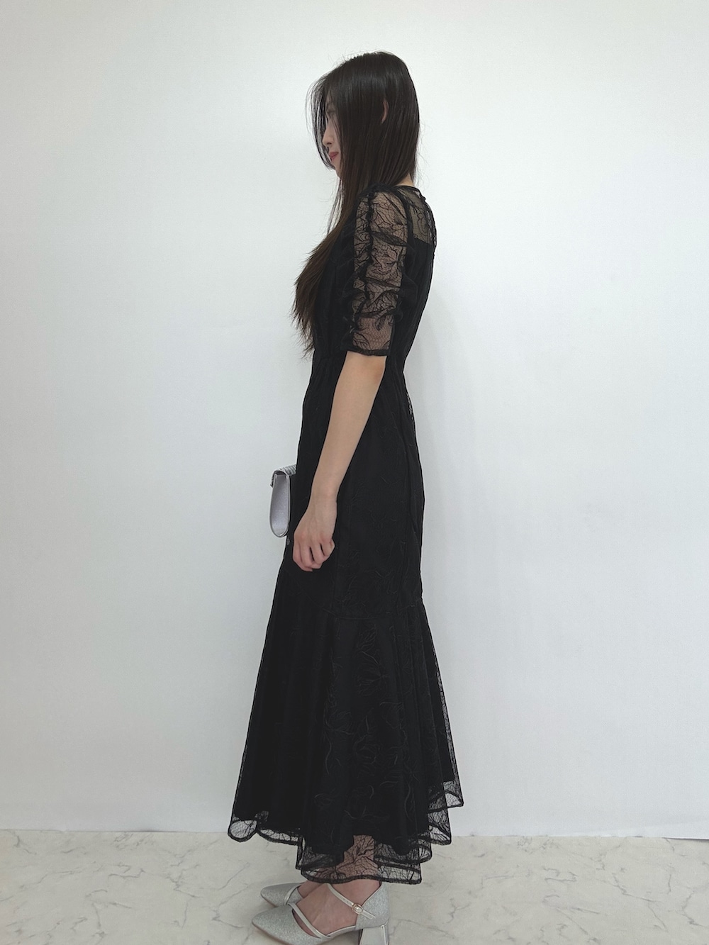 ブラック系のドレス、シルバー系のクラッチバッグ、シルバー系のパンプスを着用したレディースの秋コーディネートの2枚目の写真