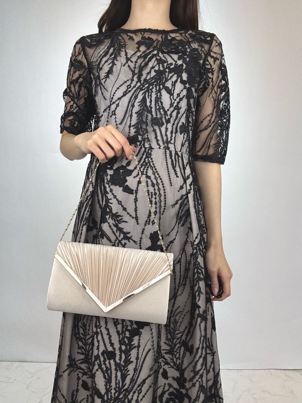 ブラック系のドレス、ベージュ系のパンプス、ベージュ系のクラッチバッグを着用したレディースの秋コーディネートの2枚目の写真