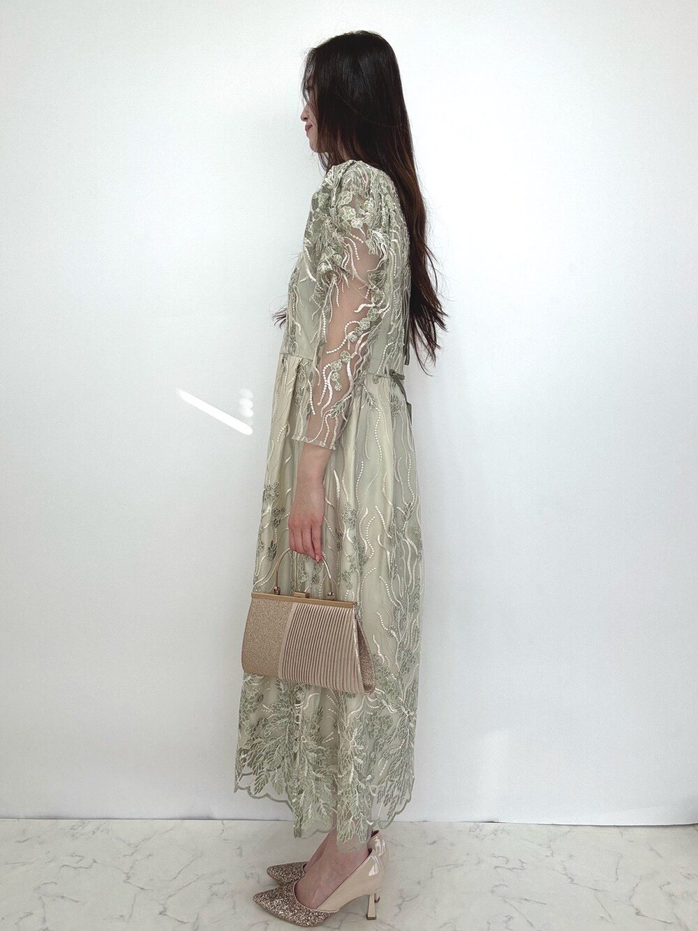 グリーン系のドレス、ベージュ系のクラッチバッグ、ベージュ系のパンプスを着用したレディースの秋コーディネートの5枚目の写真