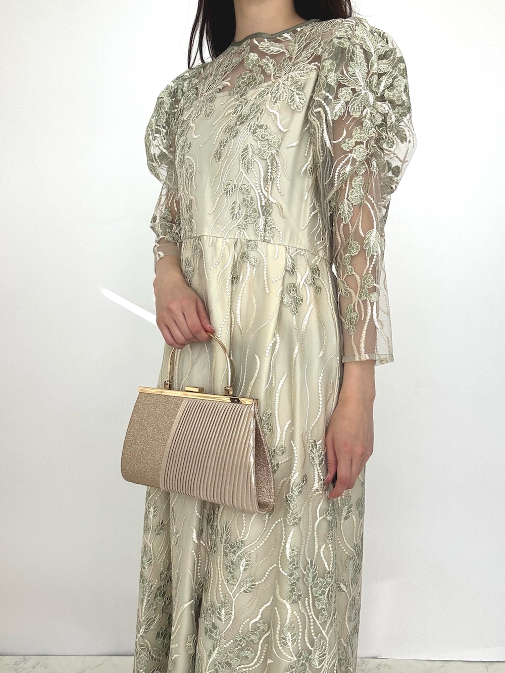 グリーン系のドレス、ベージュ系のクラッチバッグ、ベージュ系のパンプスを着用したレディースの秋コーディネートの2枚目の写真