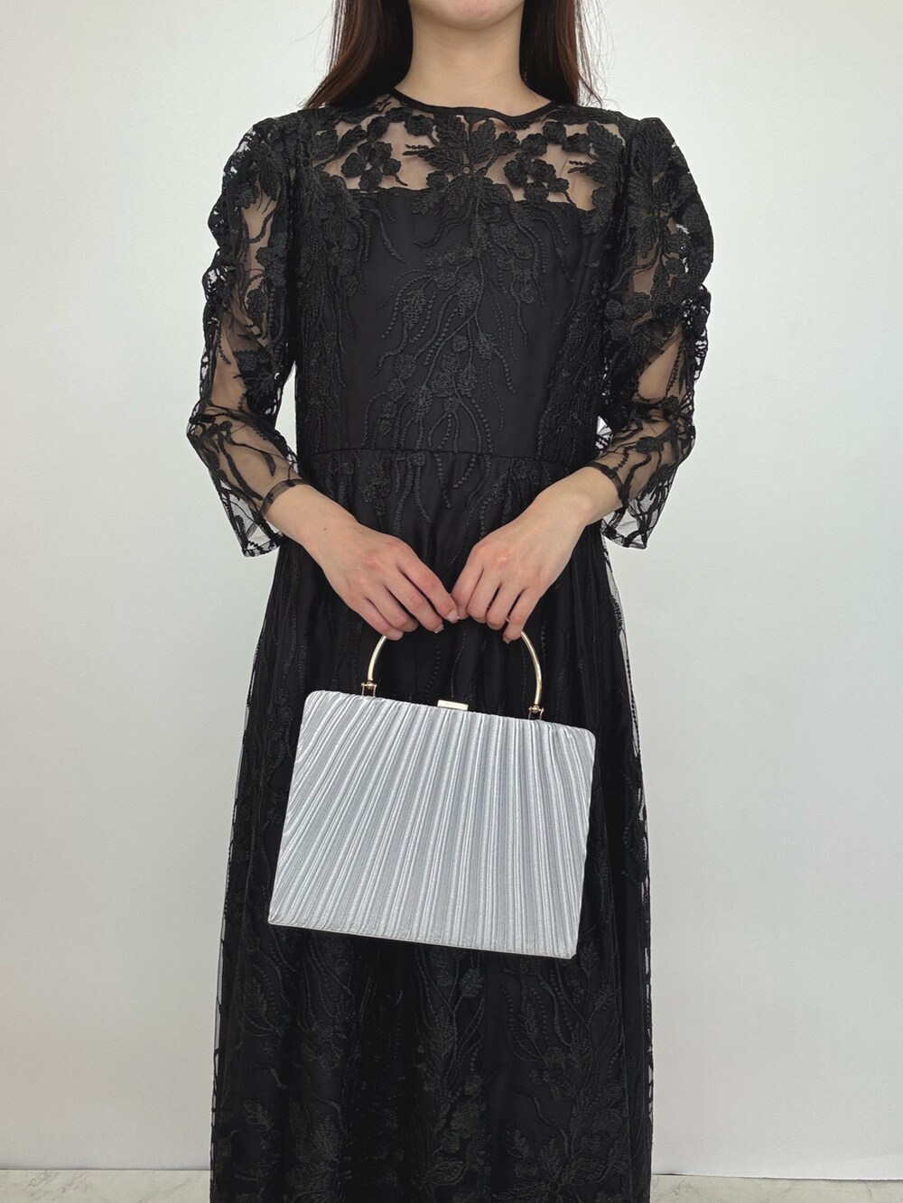 ブラック系のドレス、シルバー系のクラッチバッグ、シルバー系のパンプスを着用したレディースの秋コーディネートの4枚目の写真