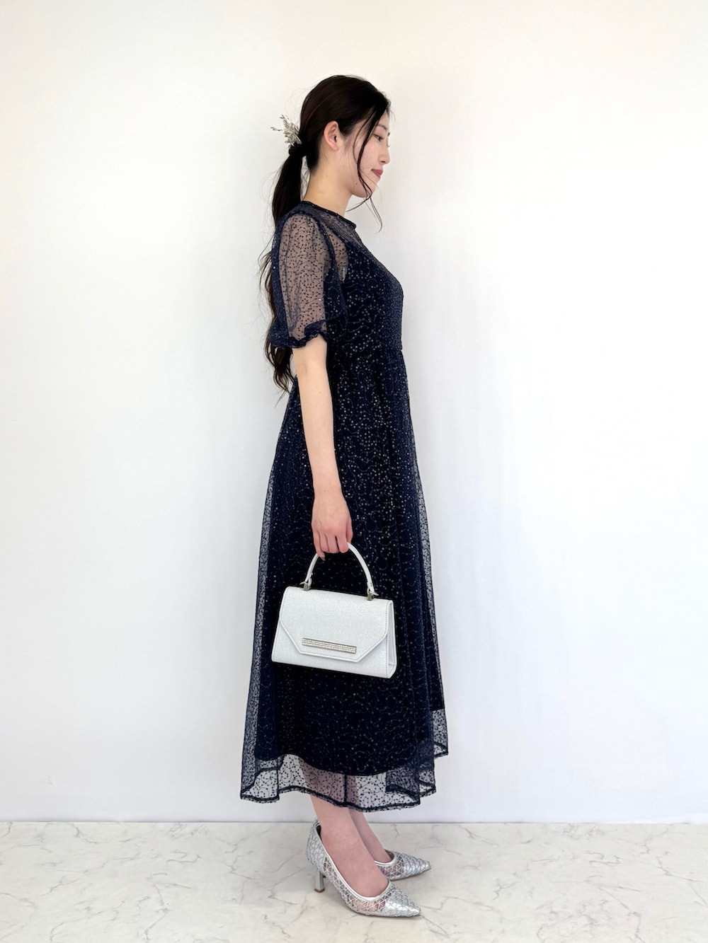 シルバー系のクラッチバッグ、ブルー系のドレス、シルバー系のパンプスを着用したレディースの夏コーディネートの4枚目の写真
