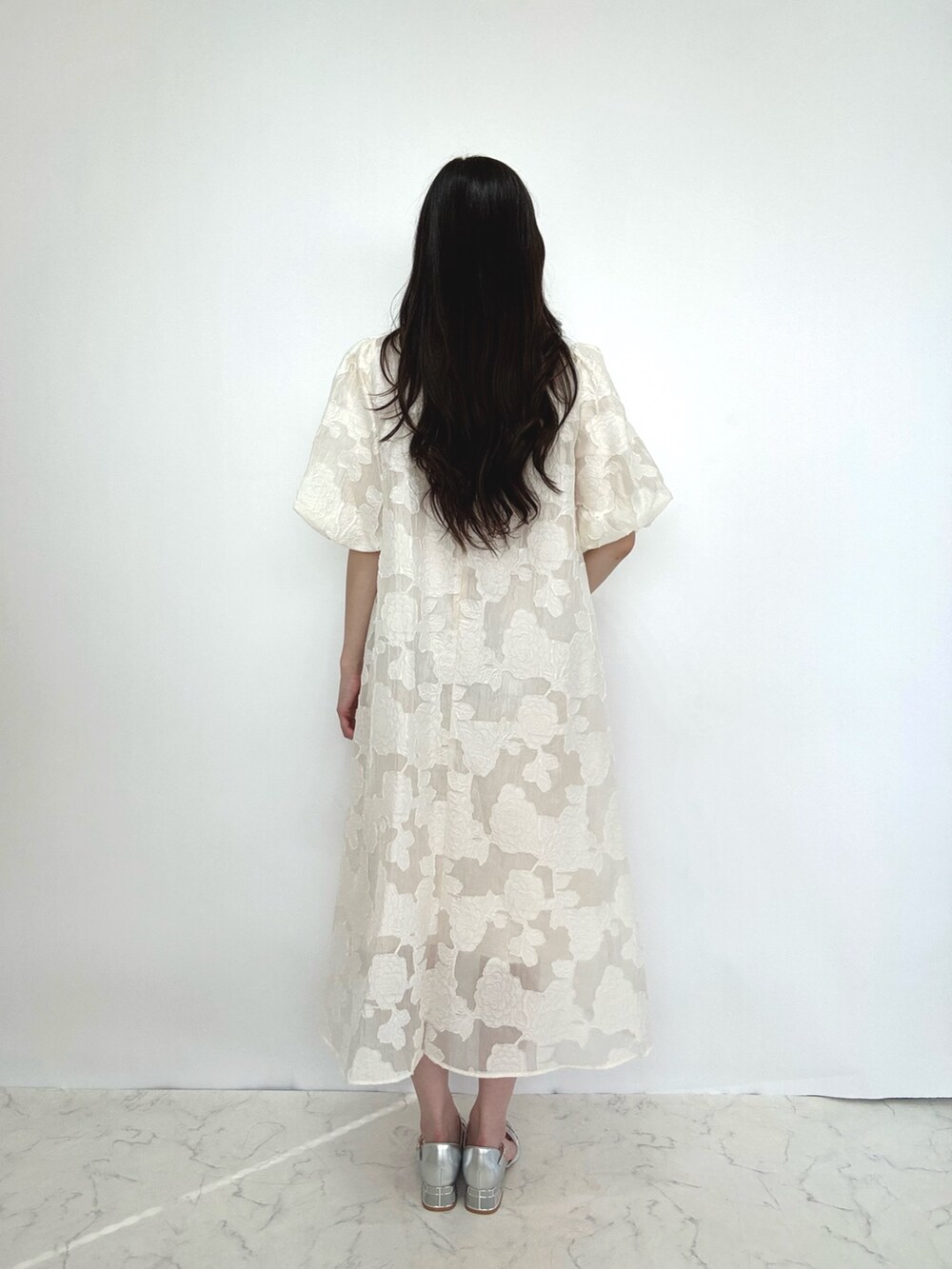 ベージュ系のドレス、ベージュ系のクラッチバッグ、シルバー系のパンプスを着用したレディースの秋コーディネートの3枚目の写真