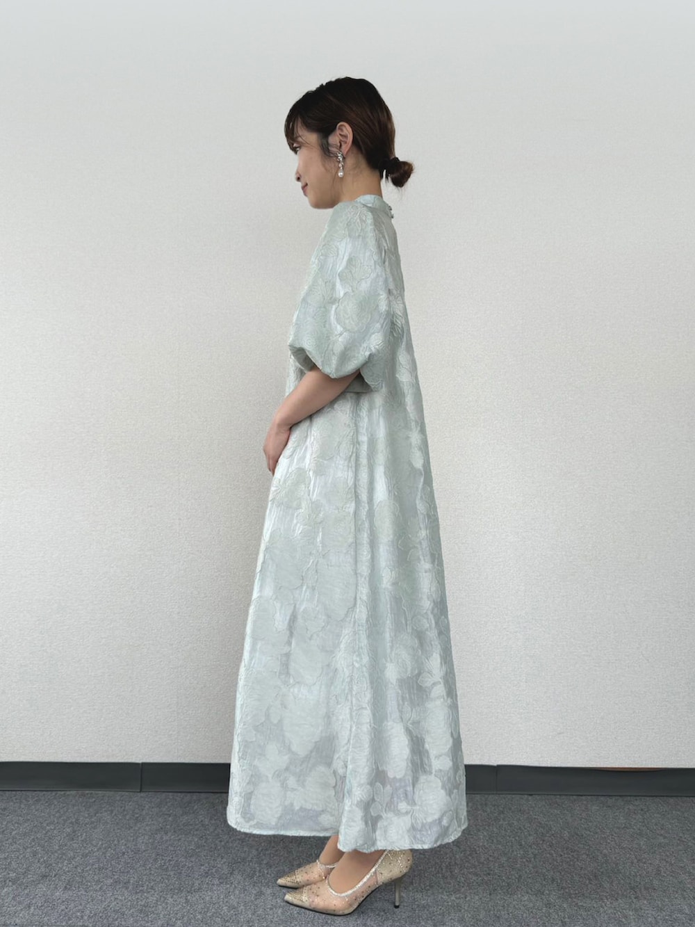 グリーン系のドレス、ベージュ系のクラッチバッグ、ゴールド系のパンプスを着用したレディースの冬コーディネートの2枚目の写真