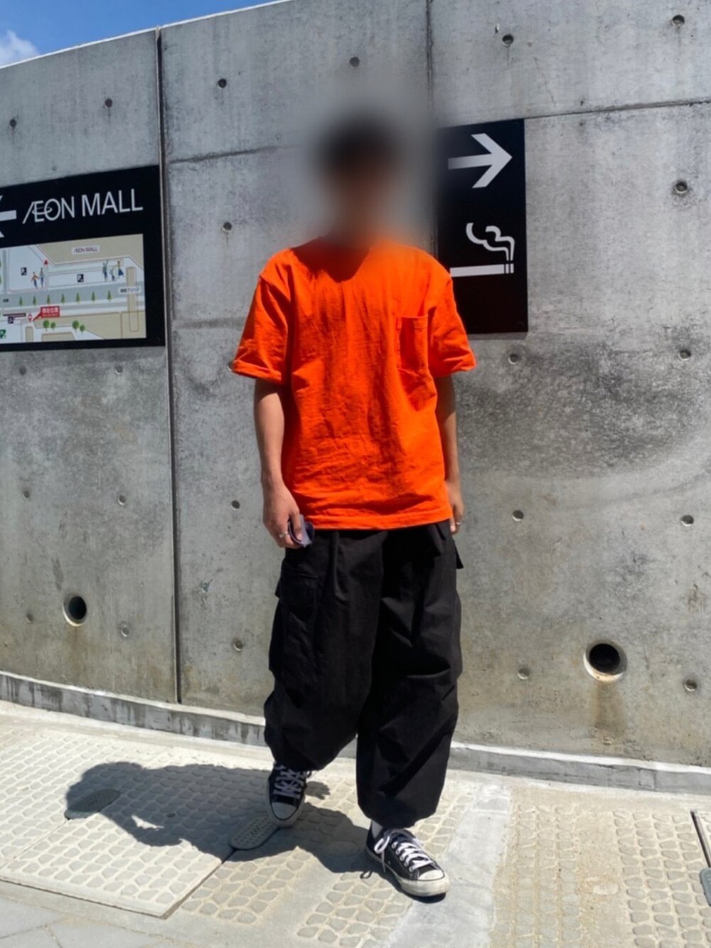 オレンジ系のTシャツ/カットソー、ブラック系のカーゴパンツ、ブラック系のスニーカーを着用したメンズの夏コーディネートの2枚目の写真