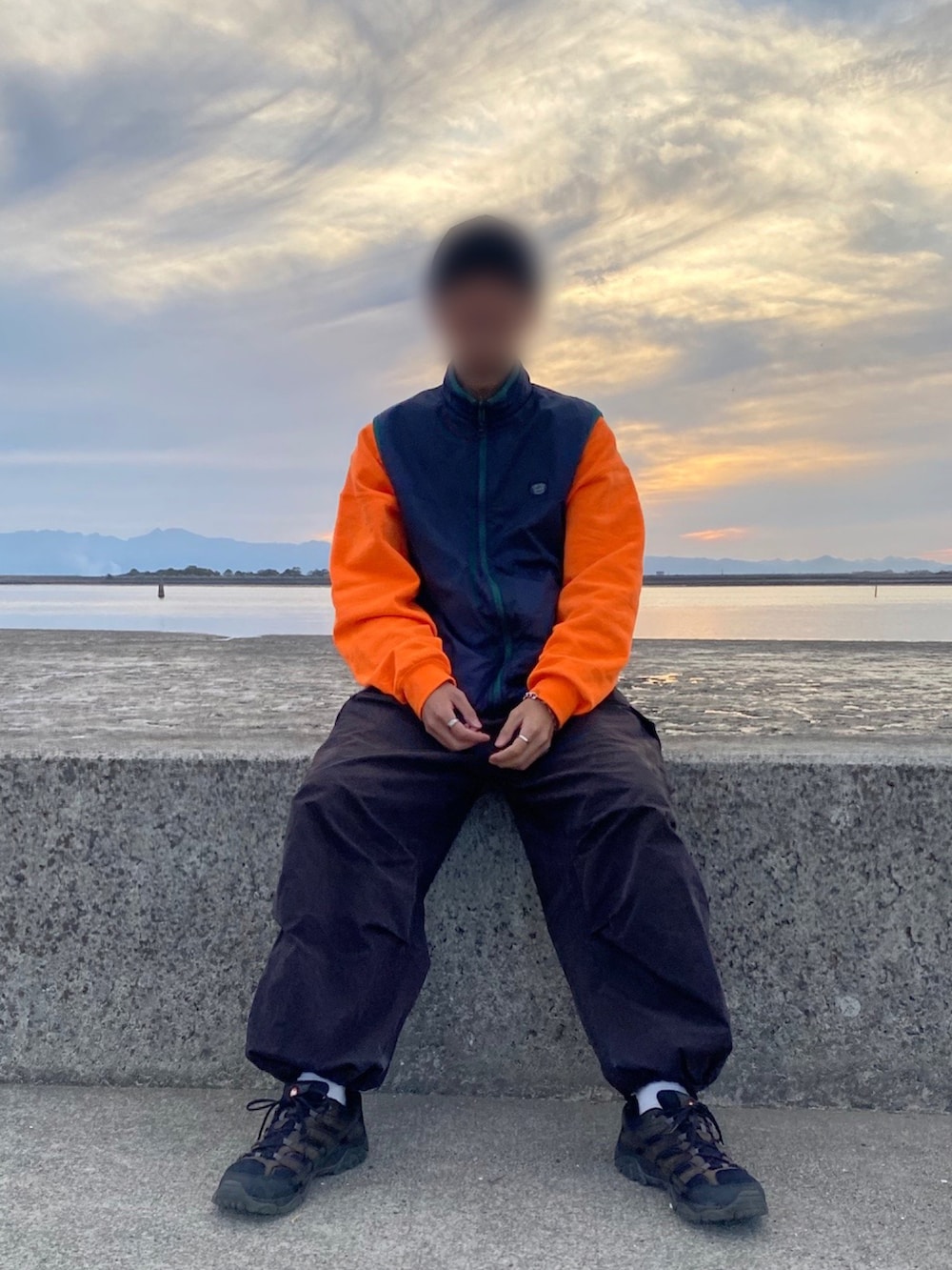 オレンジ系のスウェット、ブラック系のカーゴパンツ、ブラック系のスニーカーを着用したメンズの秋コーディネートの2枚目の写真