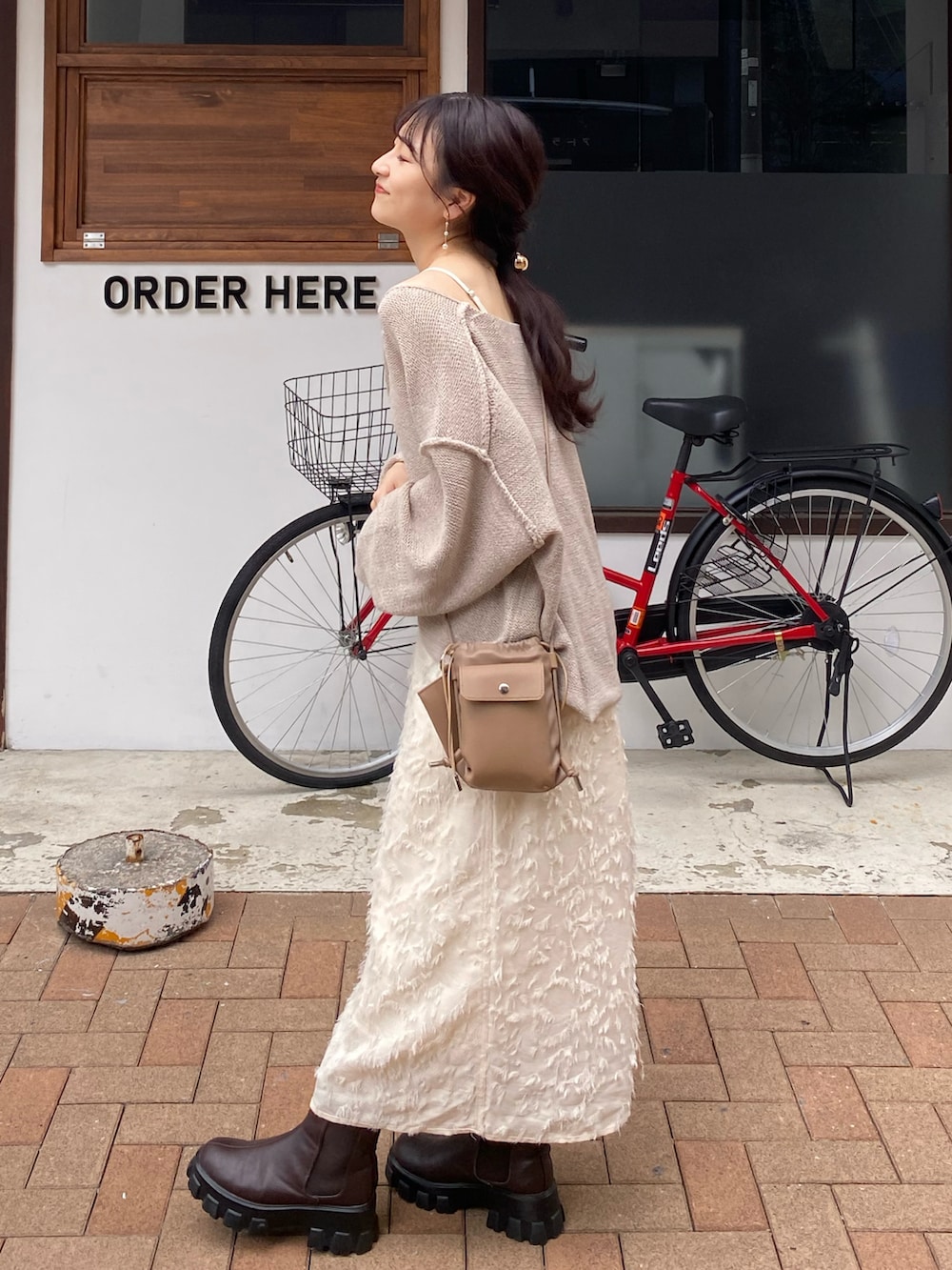 ベージュ系のショルダーバッグ、ベージュ系のニット/セーター、ホワイト系のスカートを着用したレディースの秋コーディネートの2枚目の写真