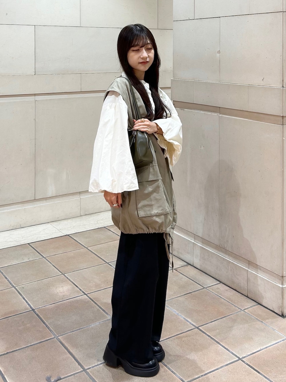 ブラック系のスラックス、ベージュ系のシャツ/ブラウス、グリーン系のトートバッグを着用したレディースの秋コーディネートの3枚目の写真