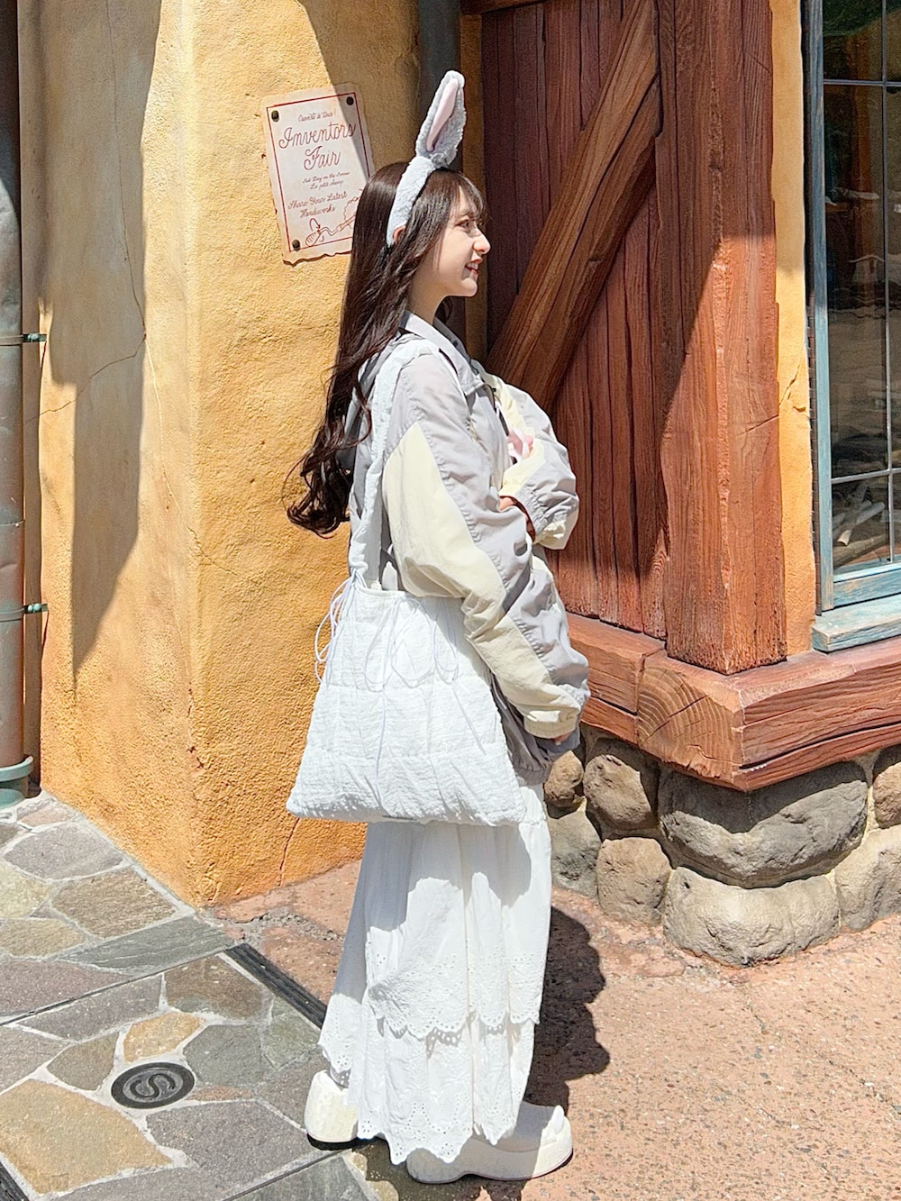 グレー系のナイロンジャケット、ホワイト系のスカート、ホワイト系のトートバッグを着用したレディースの春コーディネートの2枚目の写真