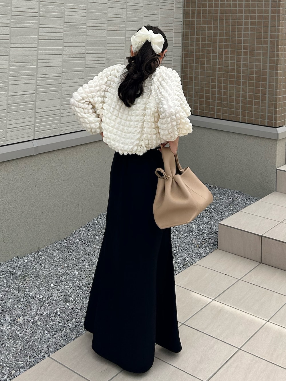 ベージュ系のバッグ、ホワイト系のTシャツ/カットソー、ブラック系のスカートを着用したレディースの春コーディネートの2枚目の写真