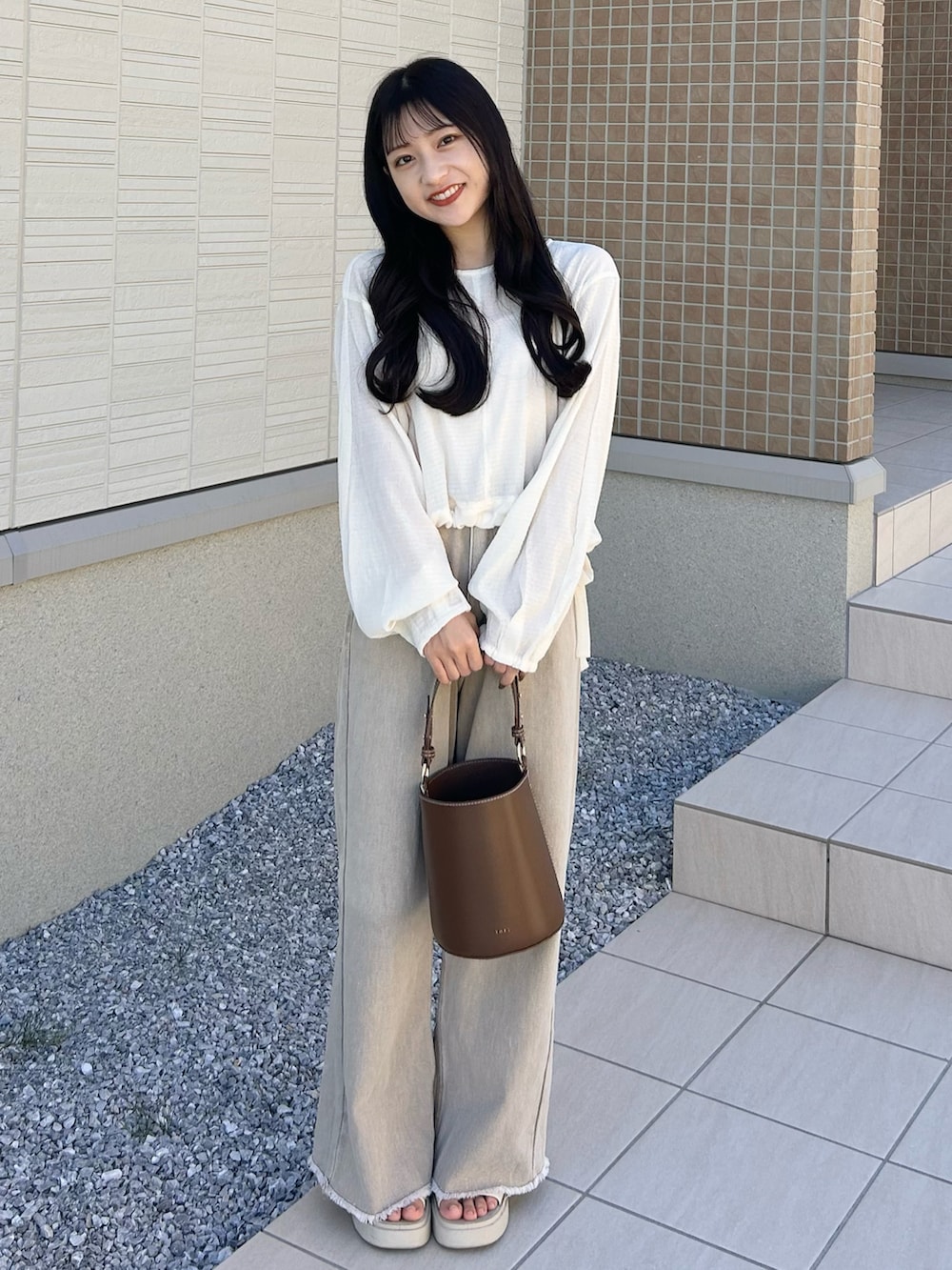 ブラウン系のハンドバッグ、ベージュ系のデニムパンツ、ホワイト系のサンダルを着用したレディースの秋コーディネートの3枚目の写真