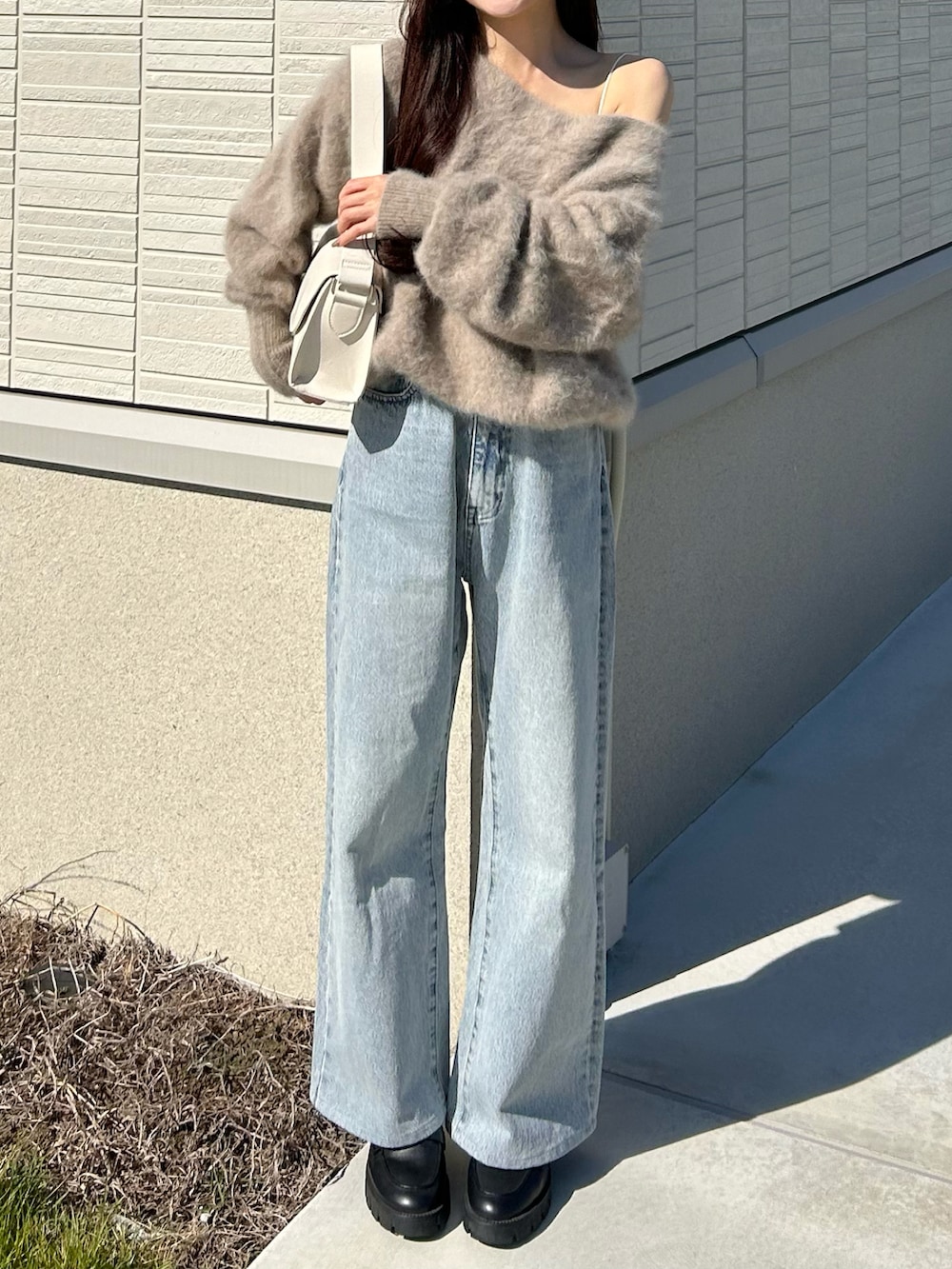 ブルー系のデニムパンツ、ブラウン系のニット/セーター、ホワイト系のショルダーバッグを着用したレディースの秋コーディネートの2枚目の写真