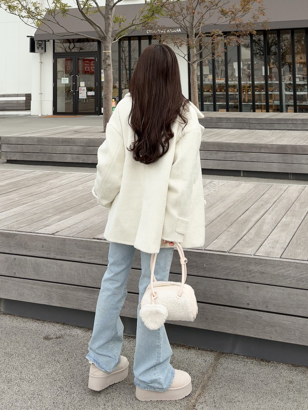 ブラウン系のカーディガン/ボレロ、ブルー系のデニムパンツ、ホワイト系のボストンバッグを着用したレディースの春コーディネートの2枚目の写真