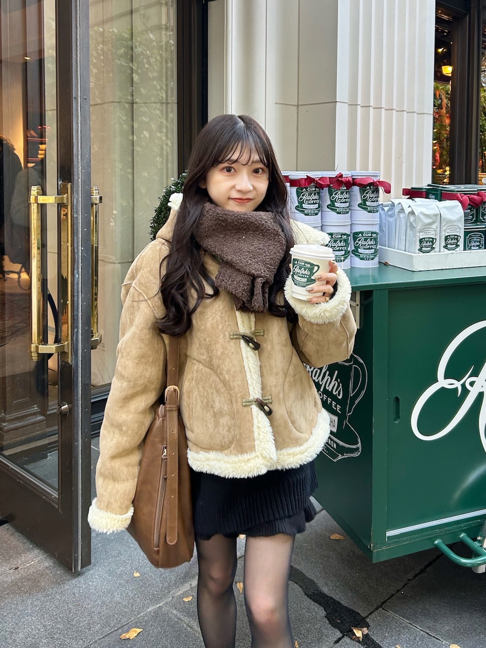 ベージュ系のムートンコート、ブラウン系のショルダーバッグ、ブラック系のニット/セーターを着用したレディースの秋コーディネートの2枚目の写真