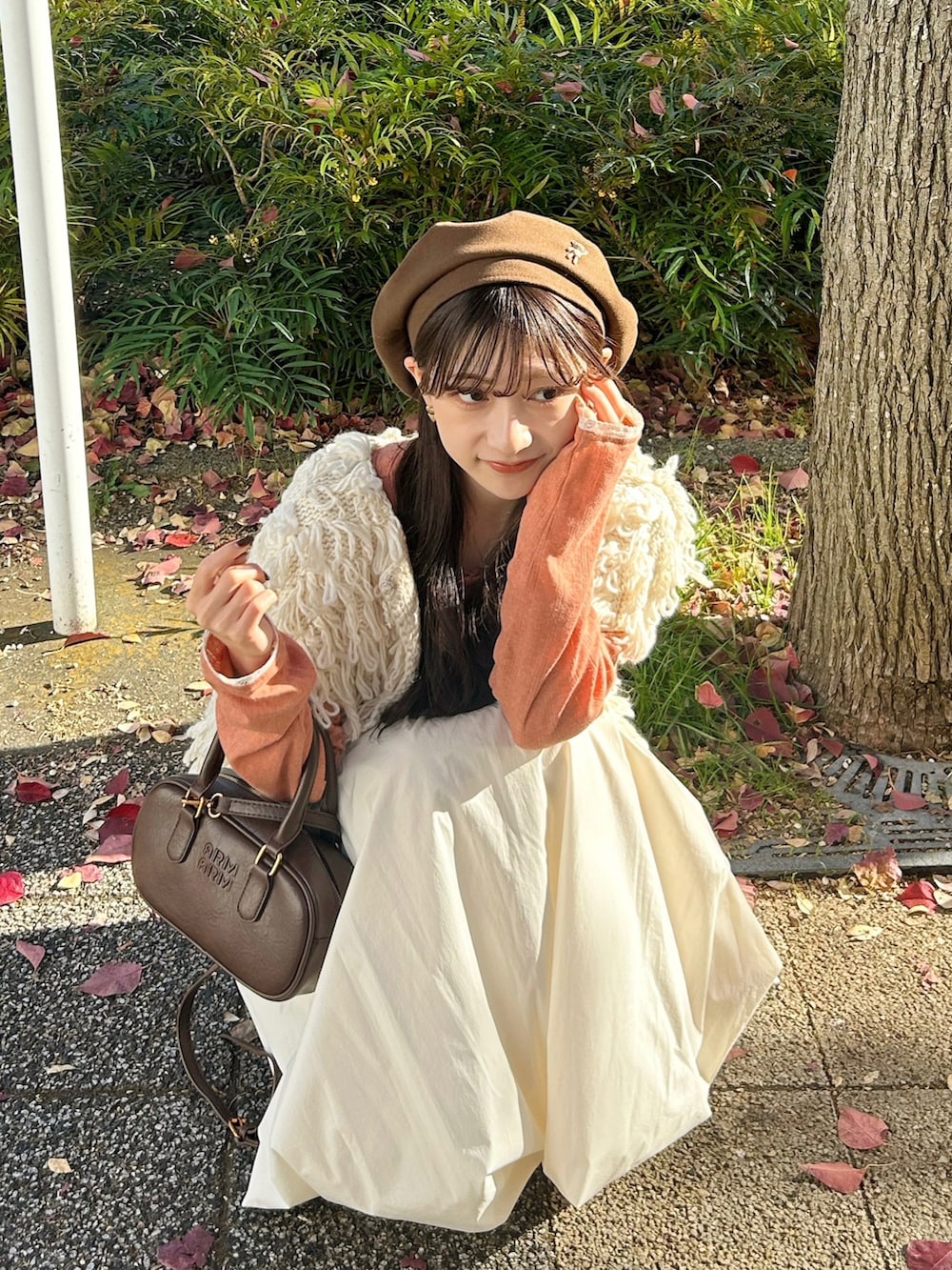 ブラウン系のバッグ、ホワイト系のスカート、ホワイト系のベストを着用したレディースの冬コーディネートの2枚目の写真