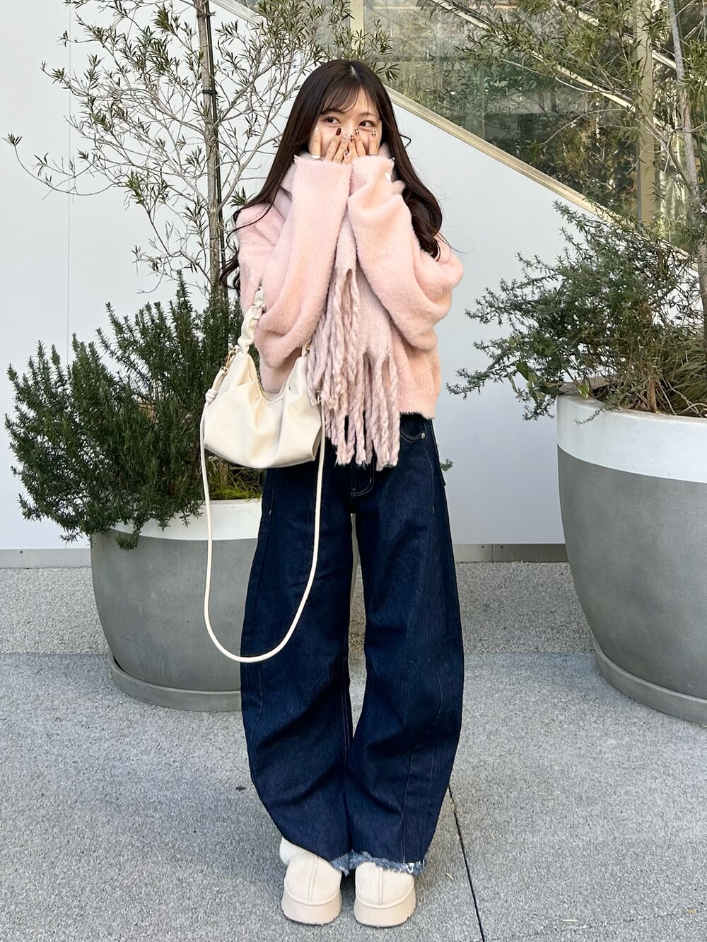 ブルー系のデニムパンツ、ピンク系のニット/セーター、ホワイト系のショルダーバッグを着用したレディースの冬コーディネートの2枚目の写真