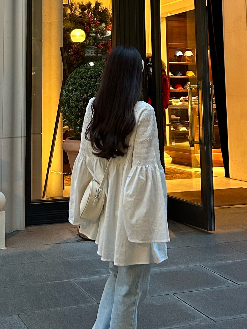 ブルー系のデニムパンツ、ホワイト系のハンドバッグ、ホワイト系のチュニックを着用したレディースの秋コーディネートの4枚目の写真