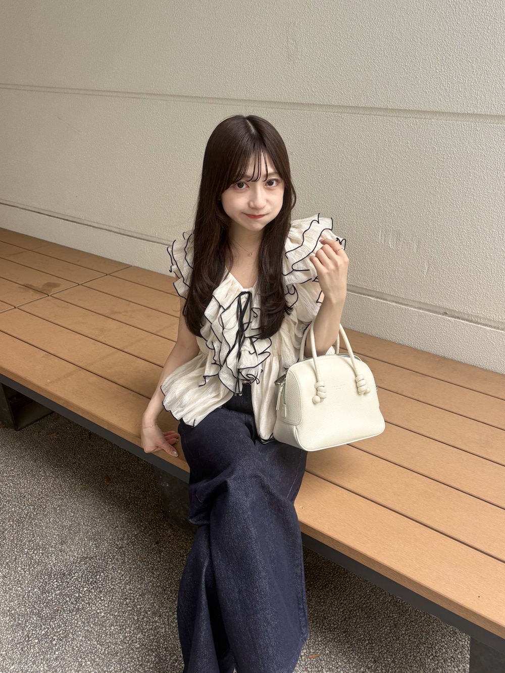 ホワイト系のハンドバッグ、ホワイト系のシャツ/ブラウス、ブルー系のデニムパンツを着用したレディースの夏コーディネートの3枚目の写真