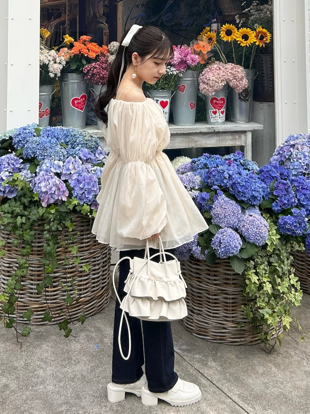 ブルー系のデニムパンツ、ホワイト系のトップス、ホワイト系のショルダーバッグを着用したレディースの春コーディネートの2枚目の写真