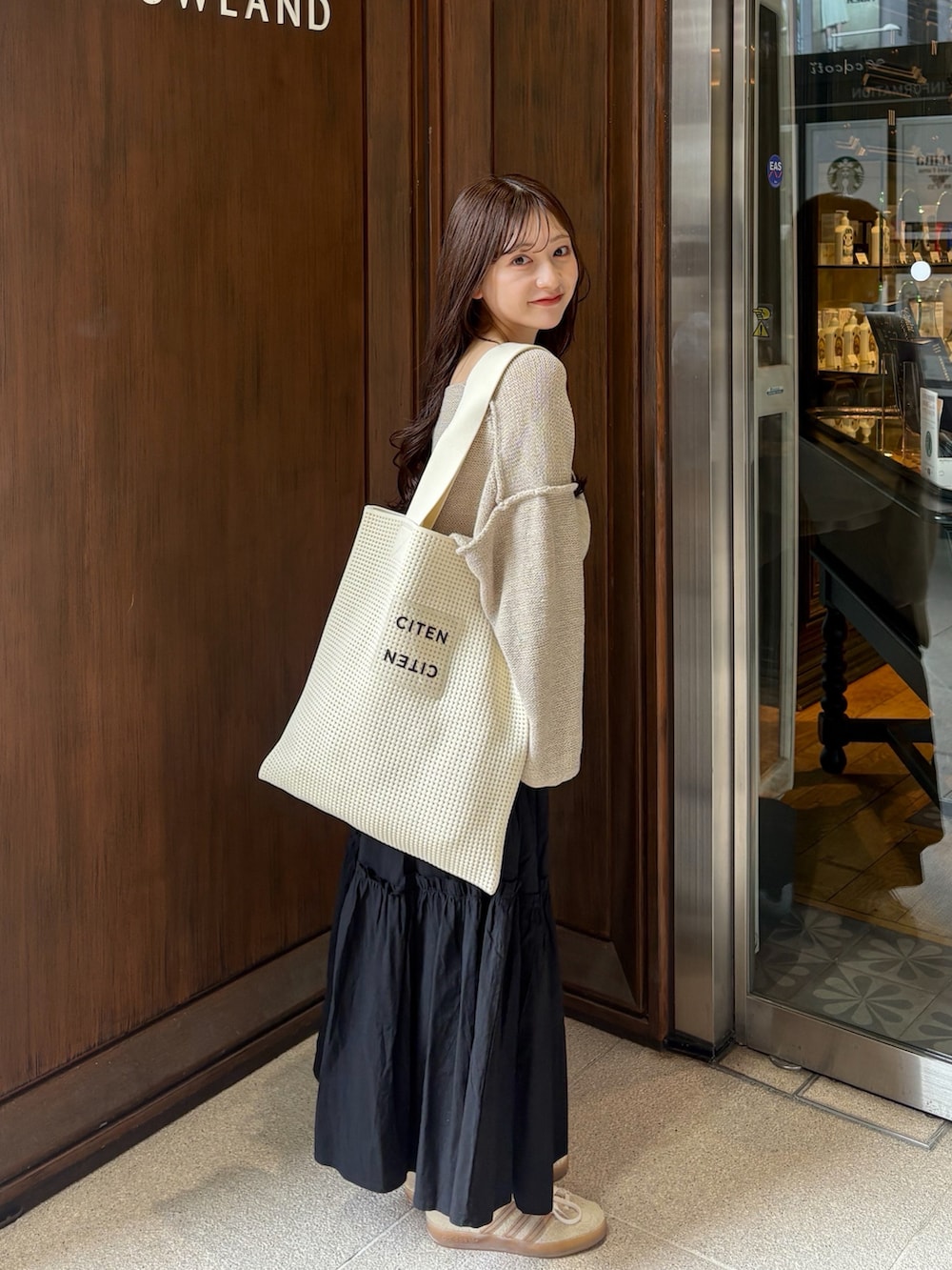 ブラック系のスカート、ベージュ系のニット/セーター、ホワイト系のトートバッグを着用したレディースの秋コーディネートの2枚目の写真