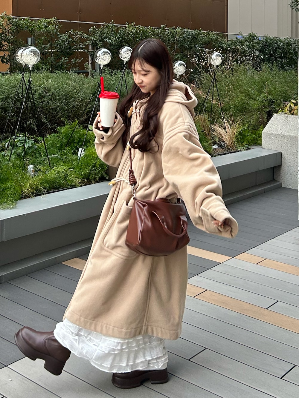 ブラウン系のボストンバッグ、ベージュ系のダッフルコート、ブラウン系のブーツを着用したレディースの冬コーディネートの2枚目の写真