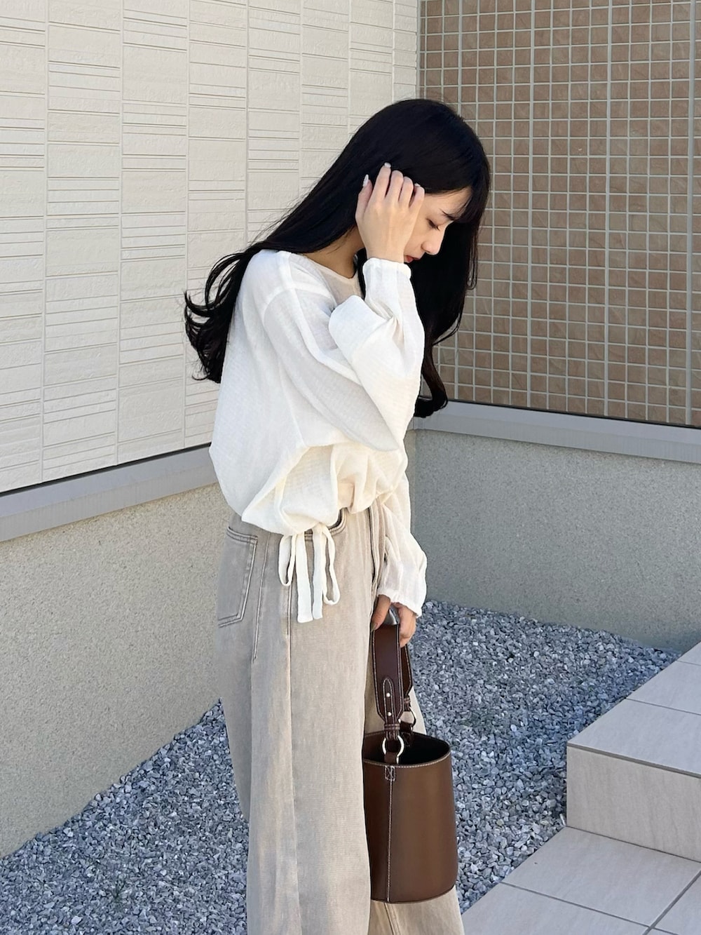 ブラウン系のハンドバッグ、ベージュ系のデニムパンツ、ホワイト系のサンダルを着用したレディースの秋コーディネートの4枚目の写真