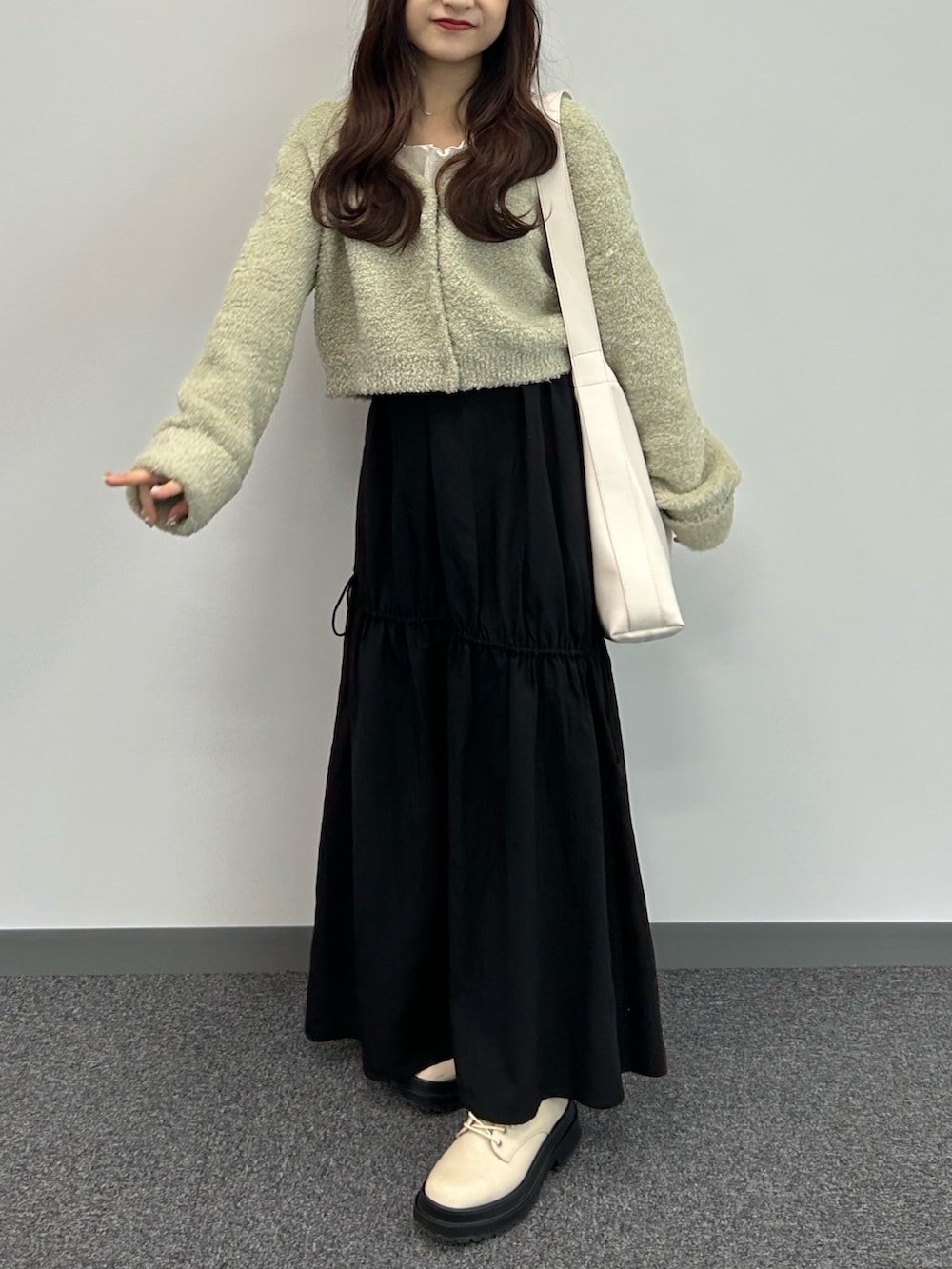 グリーン系のカーディガン/ボレロ、ブラック系のスカート、ホワイト系のトートバッグを着用したレディースの秋コーディネートの3枚目の写真
