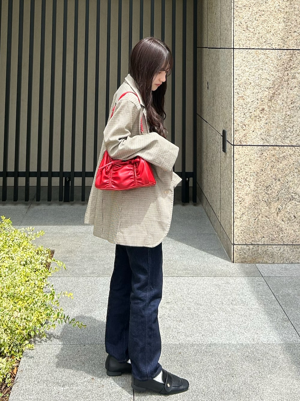 ブルー系のデニムパンツ、ベージュ系のテーラードジャケット、レッド系のショルダーバッグを着用したレディースの夏コーディネートの2枚目の写真