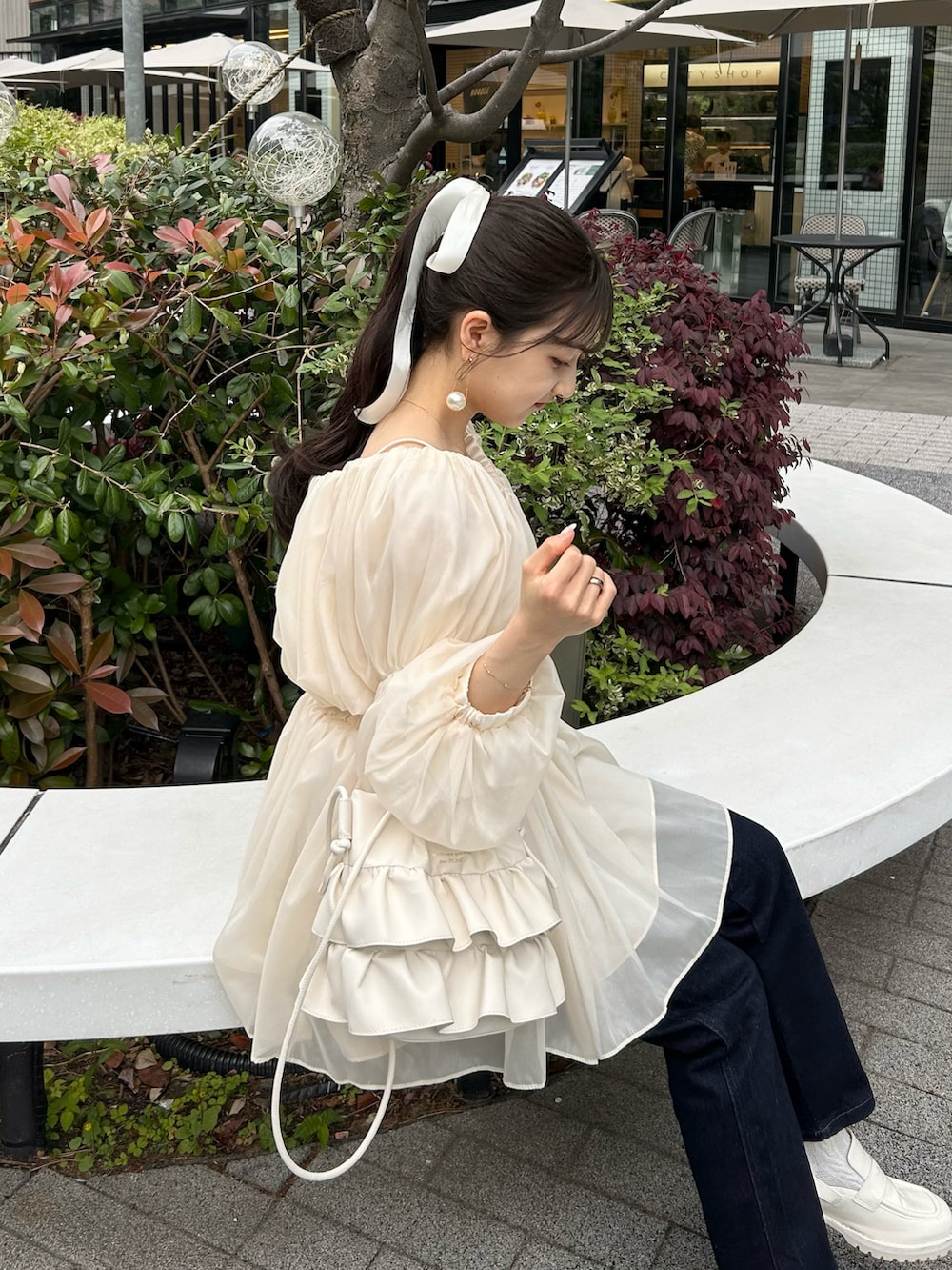 ブルー系のデニムパンツ、ホワイト系のトップス、ホワイト系のショルダーバッグを着用したレディースの春コーディネートの4枚目の写真