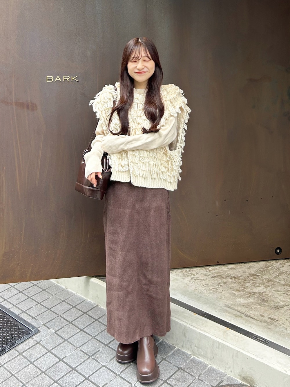 ブラウン系のスカート、ホワイト系のベスト、ホワイト系のニット/セーターを着用したレディースの秋コーディネートの2枚目の写真