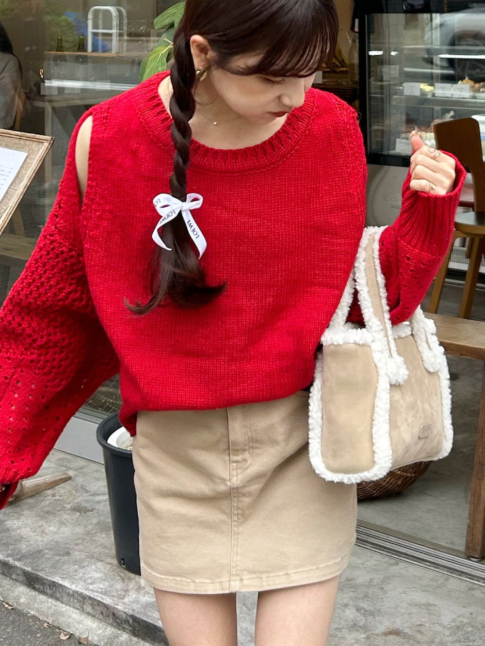 レッド系のニット/セーター、ベージュ系のデニムスカート、ベージュ系のブーツを着用したレディースの秋コーディネートの2枚目の写真