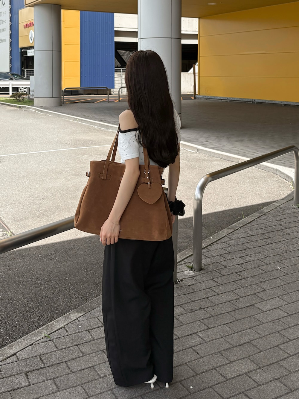 ホワイト系のサンダル、ブラック系のスラックス、ブラウン系のトートバッグを着用したレディースの夏コーディネートの2枚目の写真