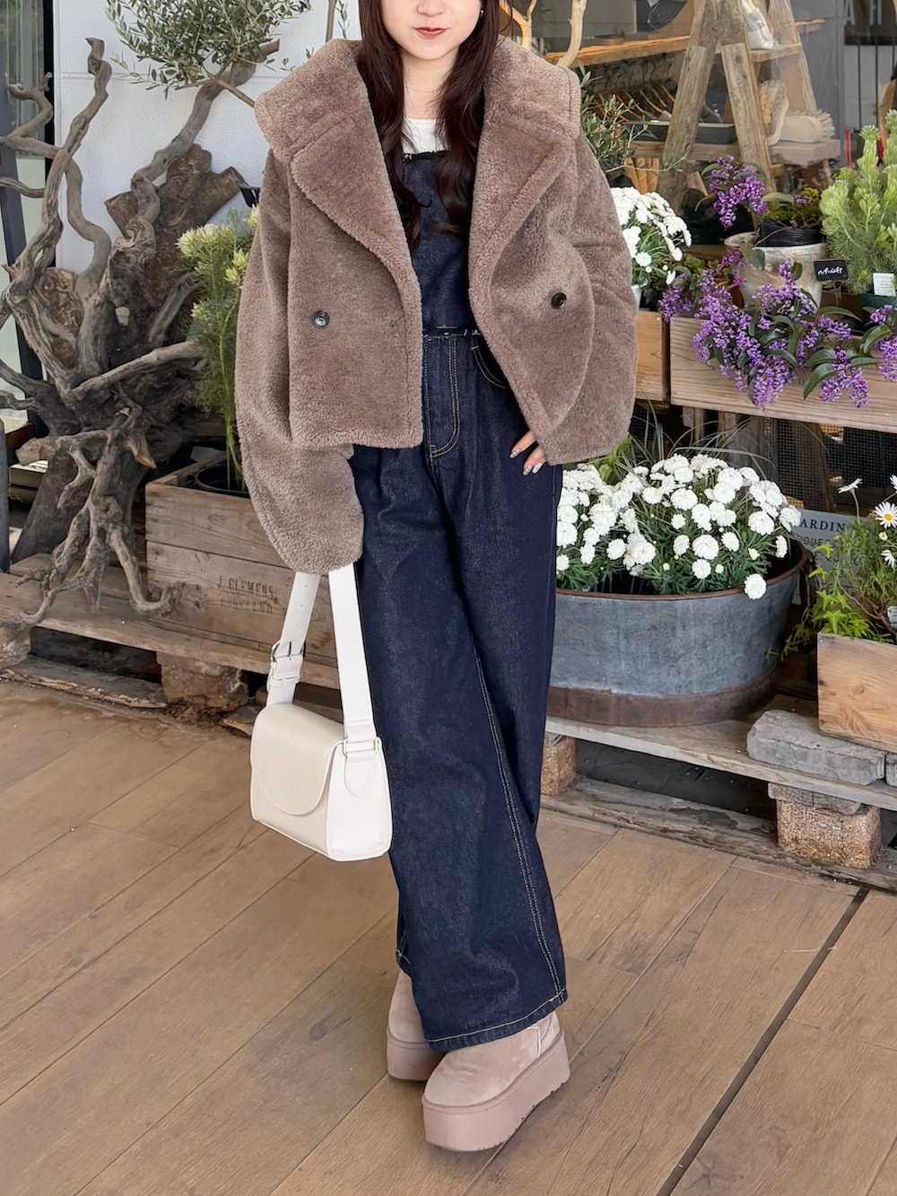 ブルー系のデニムパンツ、ブラウン系のブルゾン、ホワイト系のショルダーバッグを着用したレディースの冬コーディネートの3枚目の写真