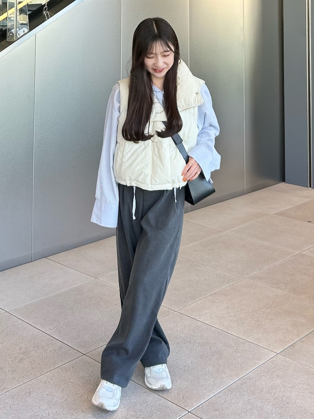 グレー系のスラックス、ホワイト系のダウンベスト、ブルー系のワンピースを着用したレディースの秋コーディネートの3枚目の写真