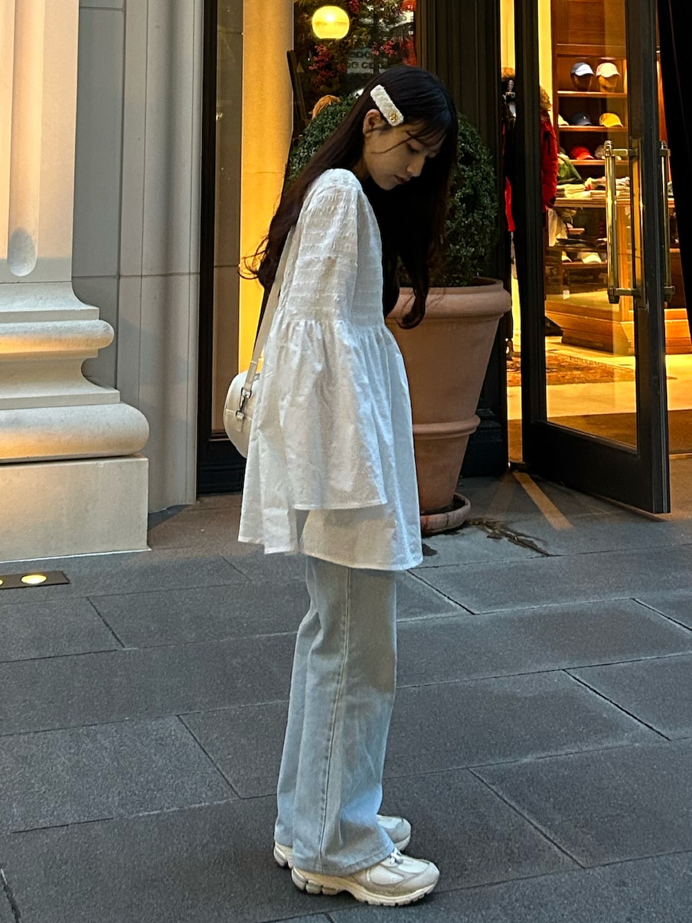 ブルー系のデニムパンツ、ホワイト系のハンドバッグ、ホワイト系のチュニックを着用したレディースの秋コーディネートの5枚目の写真