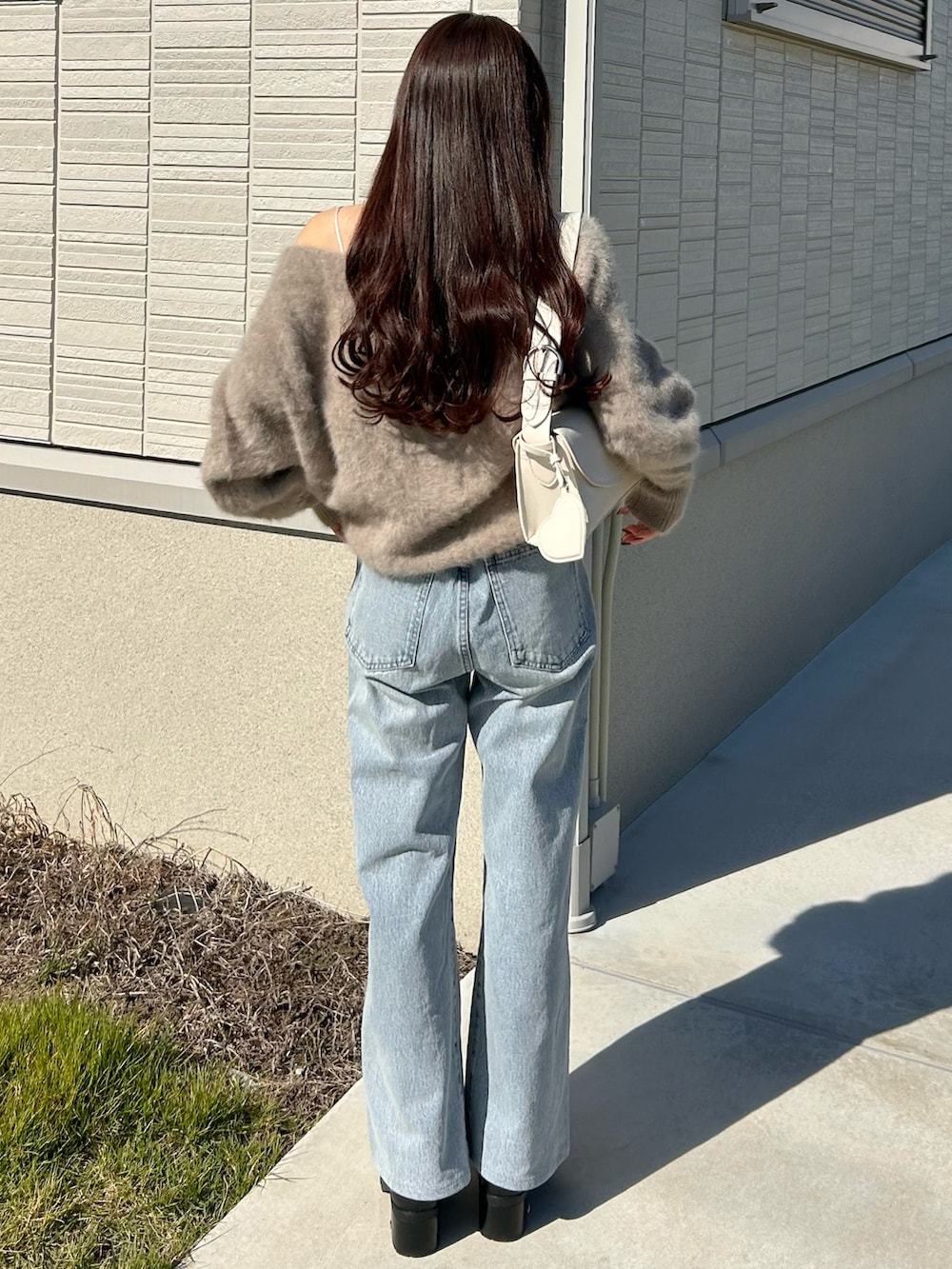 ブルー系のデニムパンツ、ブラウン系のニット/セーター、ホワイト系のショルダーバッグを着用したレディースの秋コーディネートの3枚目の写真