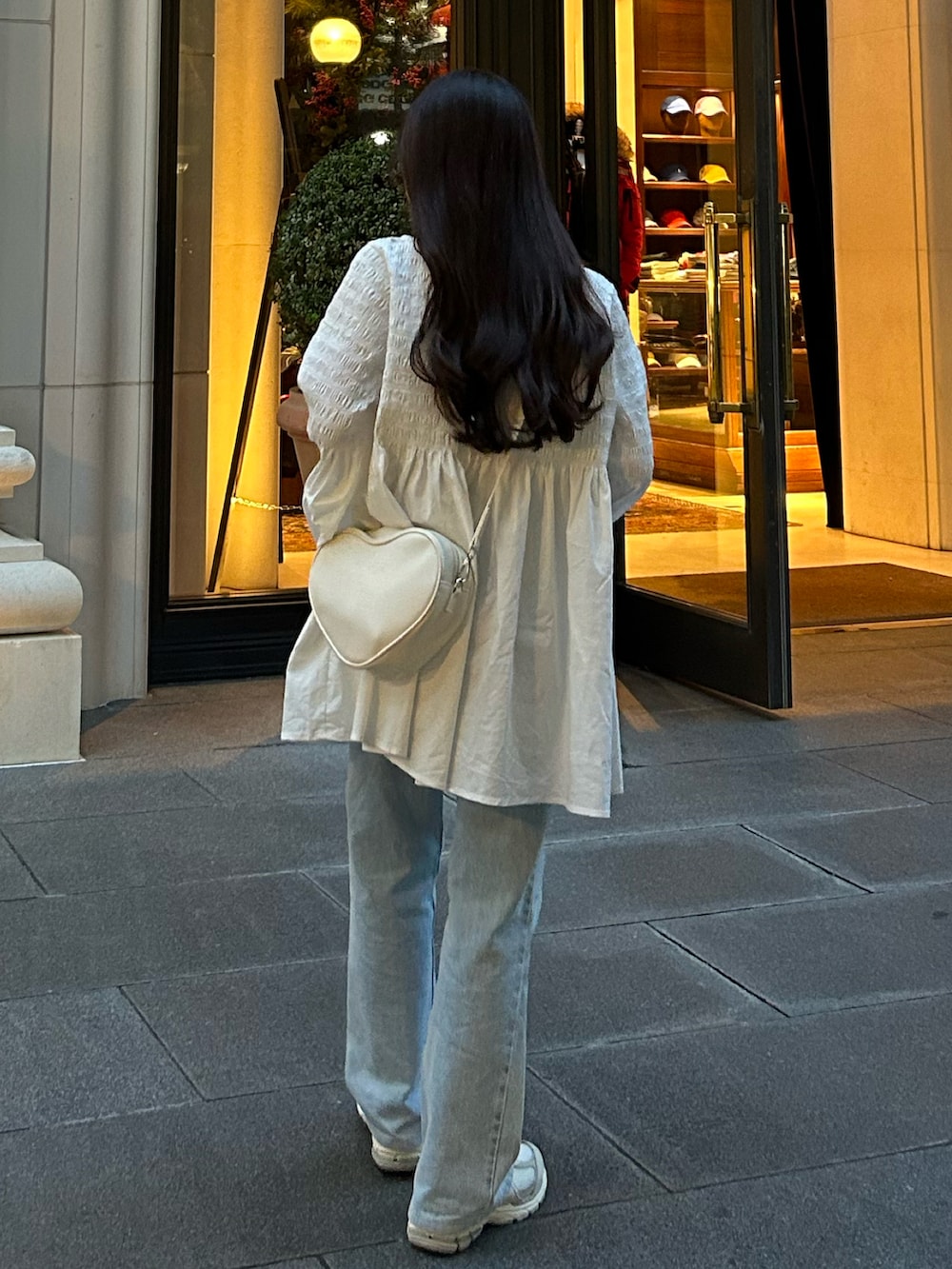 ブルー系のデニムパンツ、ホワイト系のハンドバッグ、ホワイト系のチュニックを着用したレディースの秋コーディネートの3枚目の写真