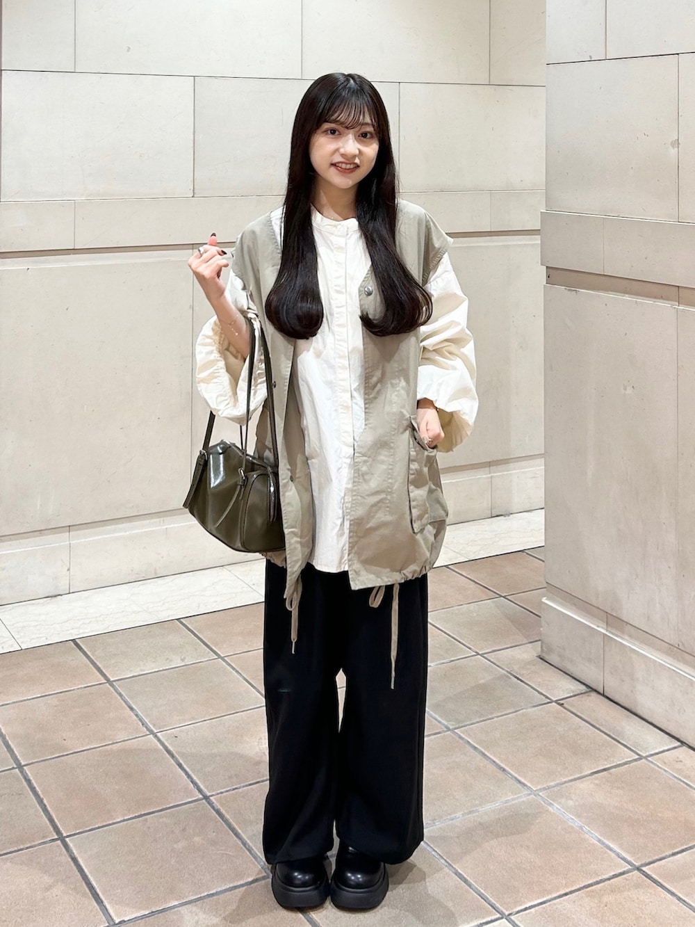 ブラック系のスラックス、ベージュ系のシャツ/ブラウス、グリーン系のトートバッグを着用したレディースの秋コーディネートの2枚目の写真