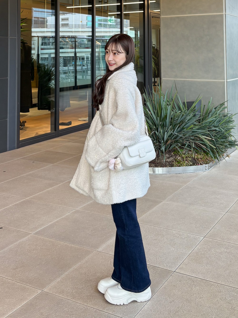 ブルー系のデニムパンツ、ホワイト系のシューズ、ホワイト系のショルダーバッグを着用したレディースの冬コーディネートの2枚目の写真